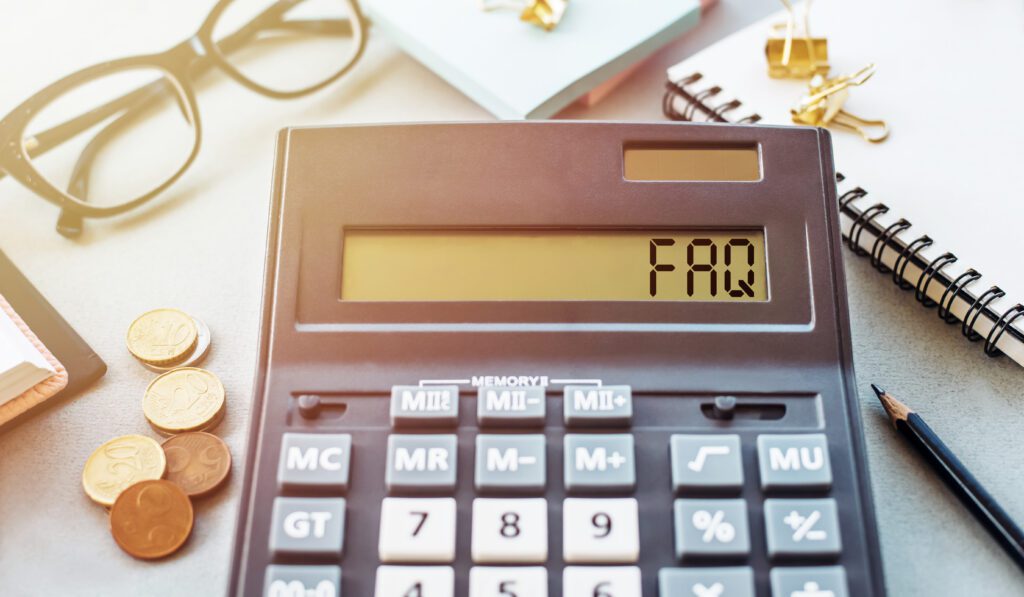 A calculator displays "FAQ" on its screen, surrounded by coins, a pencil, glasses, a notebook, and binder clips on a desk.