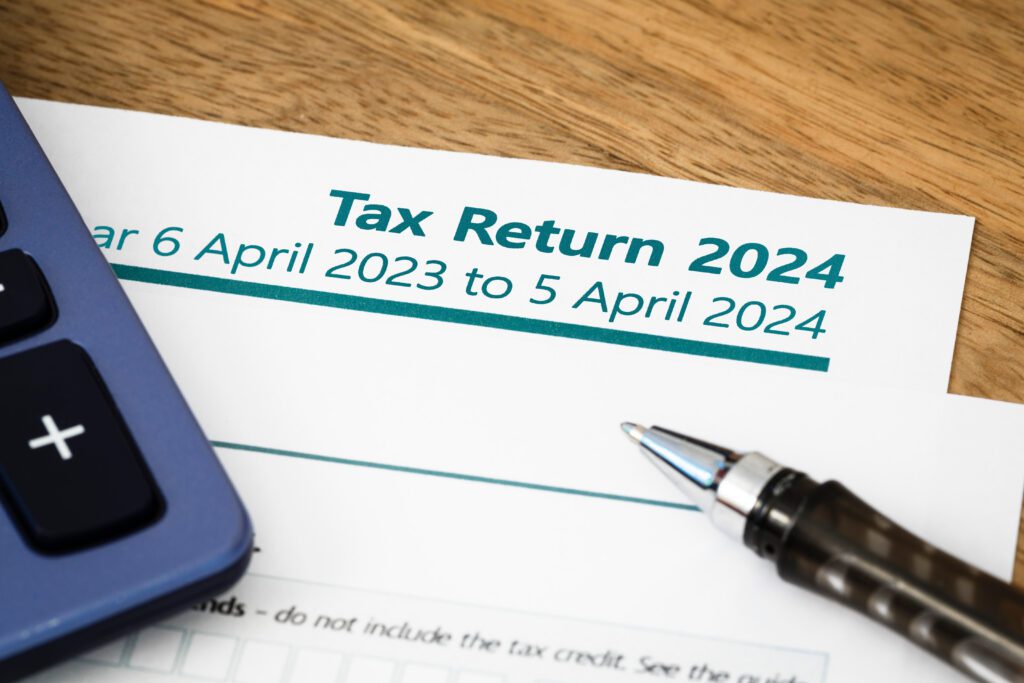 A close-up of a tax return form labeled "Tax Return 2024" for the period 6 April 2023 to 5 April 2024, next to a pen and part of a calculator on a wooden table.