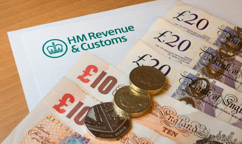 A letter from HM Revenue & Customs on a table with British pound notes (£10, £20) and coins placed on top.