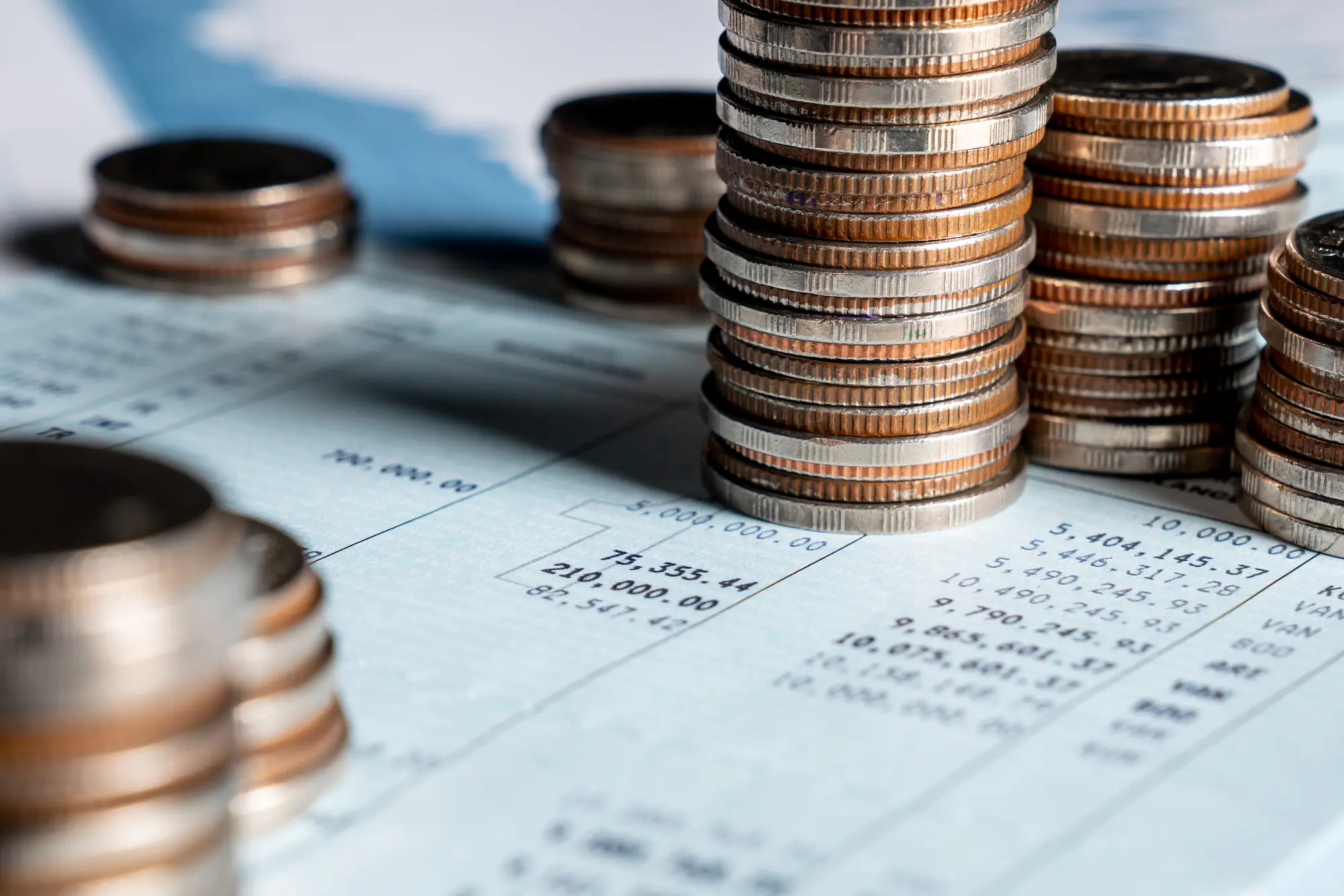 Stacks of coins are placed on top of financial documents with printed numbers and tables, suggesting themes of money, savings, or financial analysis.